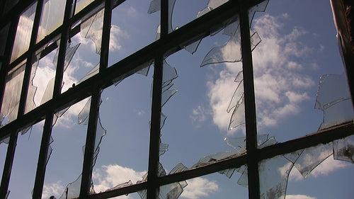 Broken window with shards of glass. Clouds move by in blue sky. HD video.
