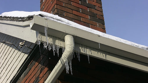Frozen eavestrough with downspout and icicles. HD video.