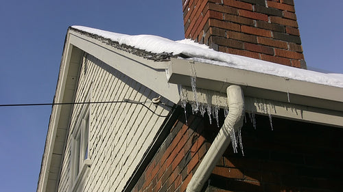 Frozen eavestrough with downspout and icicles. Wide angle. HD video.