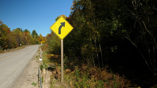 Yellow triangular road sign with corner in the distance. Wide shot. Autumn in Ontario. 4K.