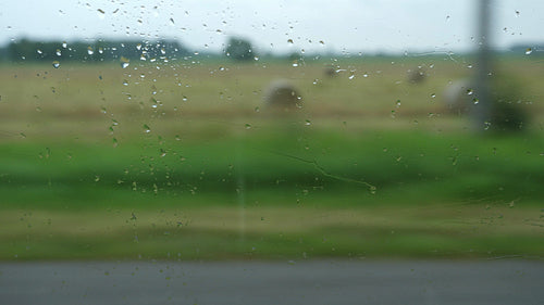Rural drive past farmers fields on rainy day. Window with drops in focus. 4K.