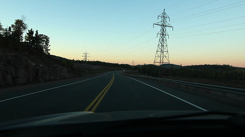 Dusk drive. Silhouettes of trees, rocks and electrical pylons. Northern Ontario. HD.