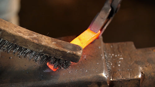 Blacksmithing. Using a wire brush and tongs to clean a red hot billet. 4K.