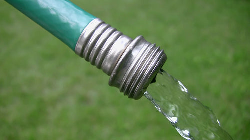 Green garden hose with water flowing. Grass background. HDV footage. HD.