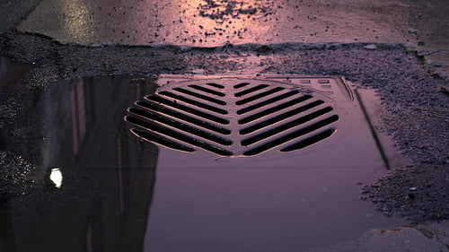 City drain with pink and purple reflection from sunset after storm. Toronto. 4K.