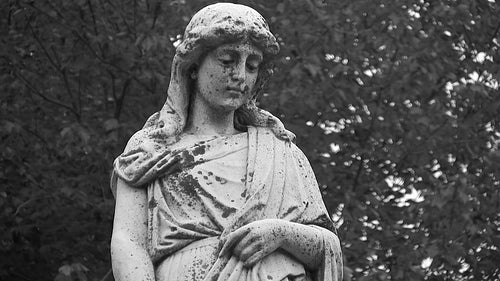 Grieving cemetery statue. Mournful figure looks downward. Black & white. HD video.