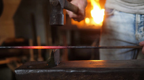 Blacksmith striking and breaking red hot metal rod with hammer on anvil. 4K.