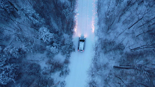 Tracking birdseye drone shot of SUV on snow covered rural road. Evening. 4K.