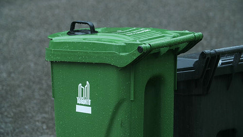 Green plastic recycling bin in the rain. Car drives by. Toronto. 4K.