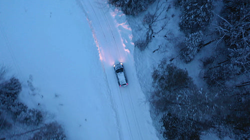 Tracking birdseye drone shot of SUV on snow covered country road. Evening. 4K.