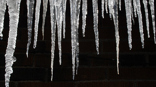 Sunlit dripping icicles on side of house. Brick background. 4K.