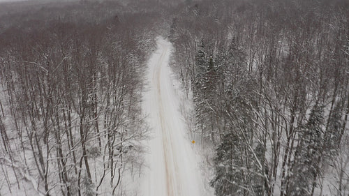 Drone following snowy rural road. Approaching corner. Snow falling. 4K.