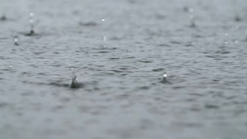 Closeup of raindrops falling on grey lake surface. Good audio of rain. 4K.