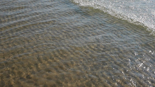 Slow motion sunlit wave with rippled sand pattern below. HD video.