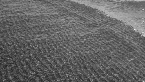 Slow motion sunlit lake waves in shallow water. Rippled sand below. Black and white. HD stock video.