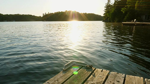 Slow motion shot of freshwater lake and sunshine with dock and cottages. Warm tint. HD.