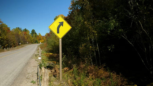 Yellow triangular road sign with corner in the distance. Wide shot. Autumn in Ontario. 4K.