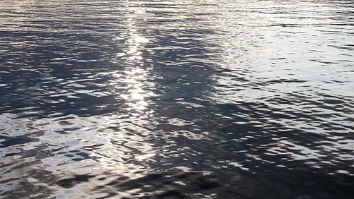 Slow motion lake water. Reflection of sparkling sun and grey clouds. HD.