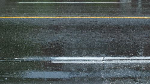 Rain on asphalt surface of road with a few cars going by. Good background for text etc. 4K.