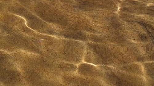 Slow motion shot of sunny reflections in clear lakewater with sandy bottom. HD.