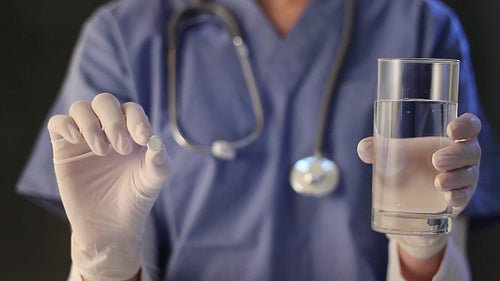 Female nurse holds up pill and water. Shallow depth of field. HD.