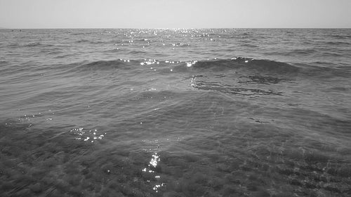 Slow motion sunlit lake with crashing wave. Rippled sand visible below. Black & white. HD video.