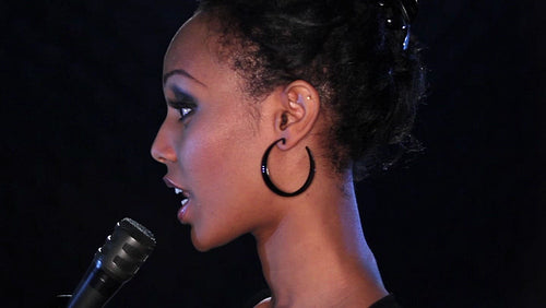 Attractive young black woman sings into a microphone. Profile. HD.