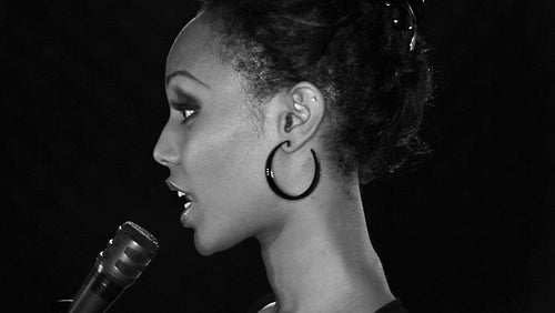 Attractive young black woman sings into a microphone. Black and white. Profile. HD.