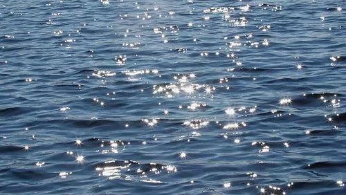 Slow motion wide shot of blue lake water. Brilliant sparkles from sun. HD.