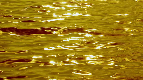 Slow motion metallic looking lake water with sunny highlights. Gold tint. HD.