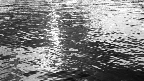 Slow motion lake water. Reflection of sparkling sun and grey clouds. Black & white. HD.