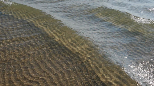 Slow motion sunlit lake waves in shallow water. Rippled sand below. HD stock video.