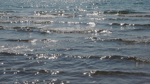 Slow motion detail of small sparkling and breaking sunlit waves. HD video.