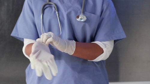 Young female nurse in blue scrubs puts on rubber gloves. HD.