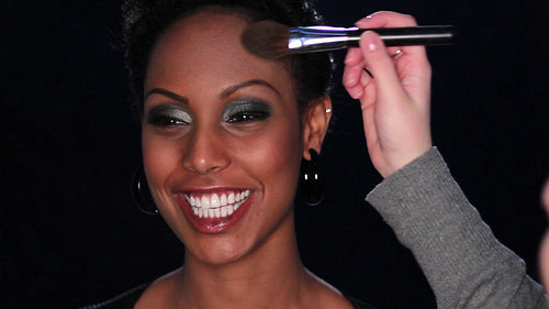 Attractive, young black female model gets made up with brush and powder. HD.