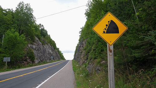 Sign warning of falling rocks with rockcut and road ahead. Ontario, Canada. 4K.