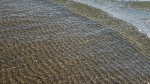 Slow motion sunlit lake waves in shallow water. Rippled sand below. HD stock video.