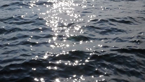 Slow motion surface of waves in blue lake. Defocused sun highlights. HD.