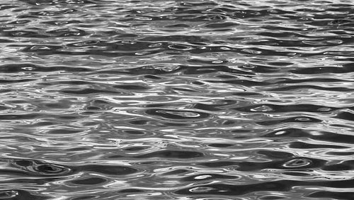 Silky smooth, slow motion lake waves. Black and white. Silver metallic look. HD.