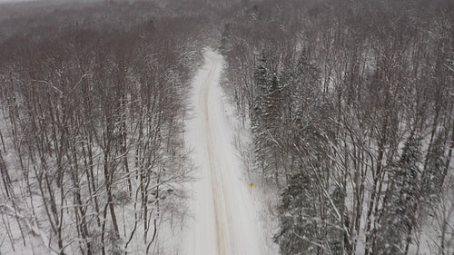 Drone following snowy rural road. Approaching corner. Snow falling. 4K.