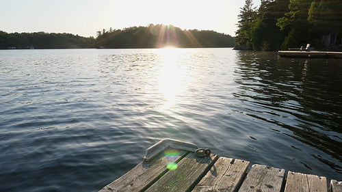 Slow motion shot of freshwater lake and sunshine with dock and cottages. HD.