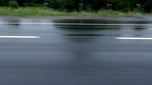 Wet highway surface with white lines, shoulder and greenery beyond. HD.