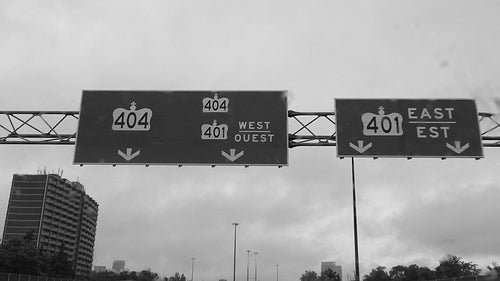 Slow motion shot in rain passing sign for Highways 404 and 401. Toronto. Black & white. HD.