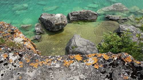 Cliff edge with orange lichen. View of rocks and water below. HD.