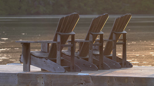 Three Muskoka chairs illuminated by the sun. Sparkling lake. Cottage country. HD.
